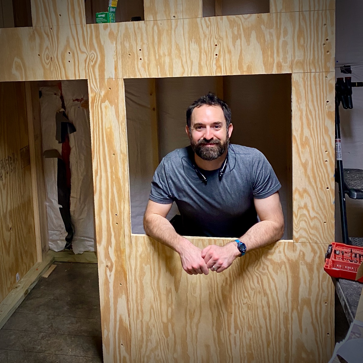 David Peterson leaning through a plywood window opening of a playhouse mid-build