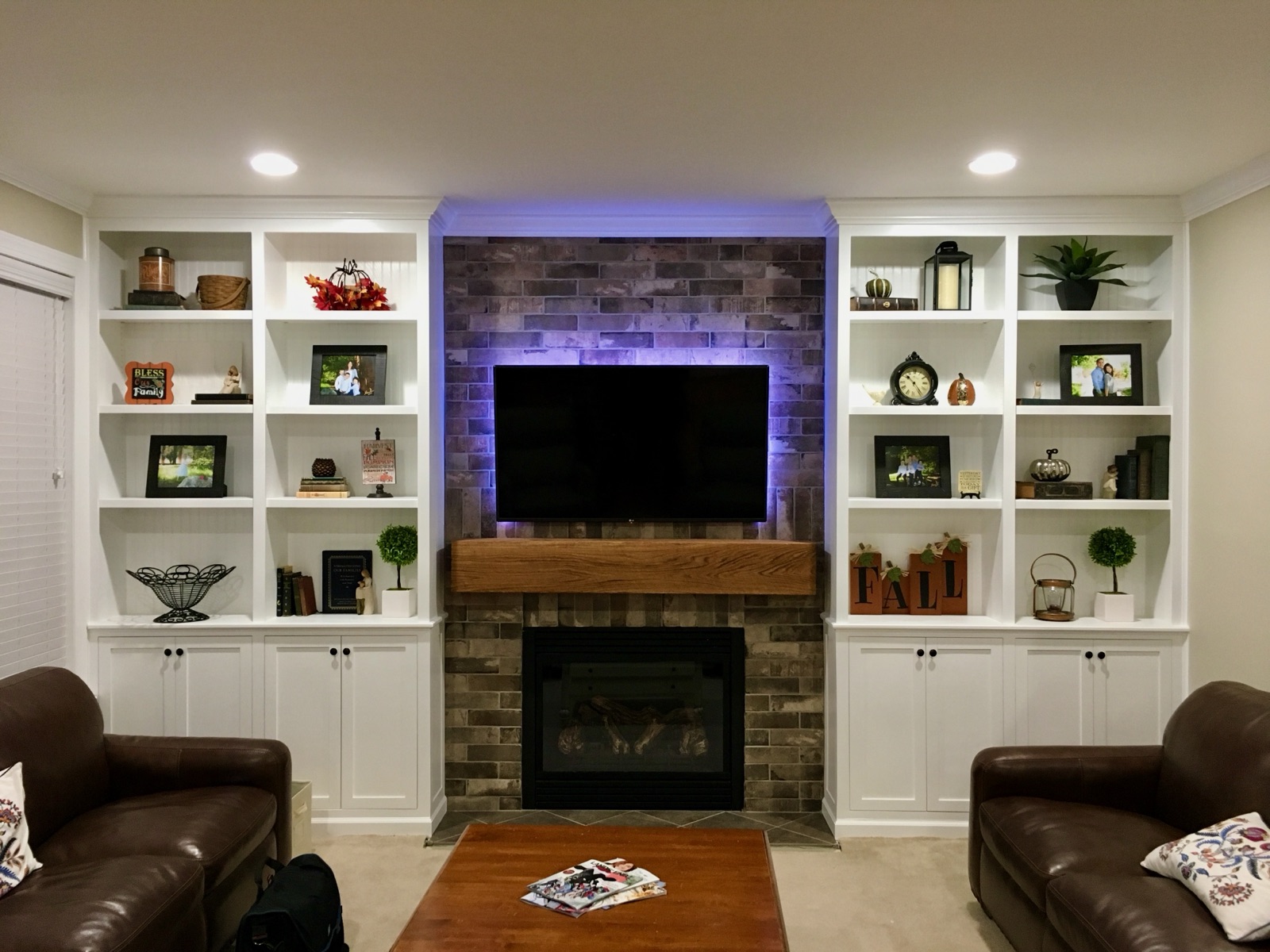 A brick-tile fireplace wall with a wall-mounted TV, accent lighting, and white built-in bookcases flanking it