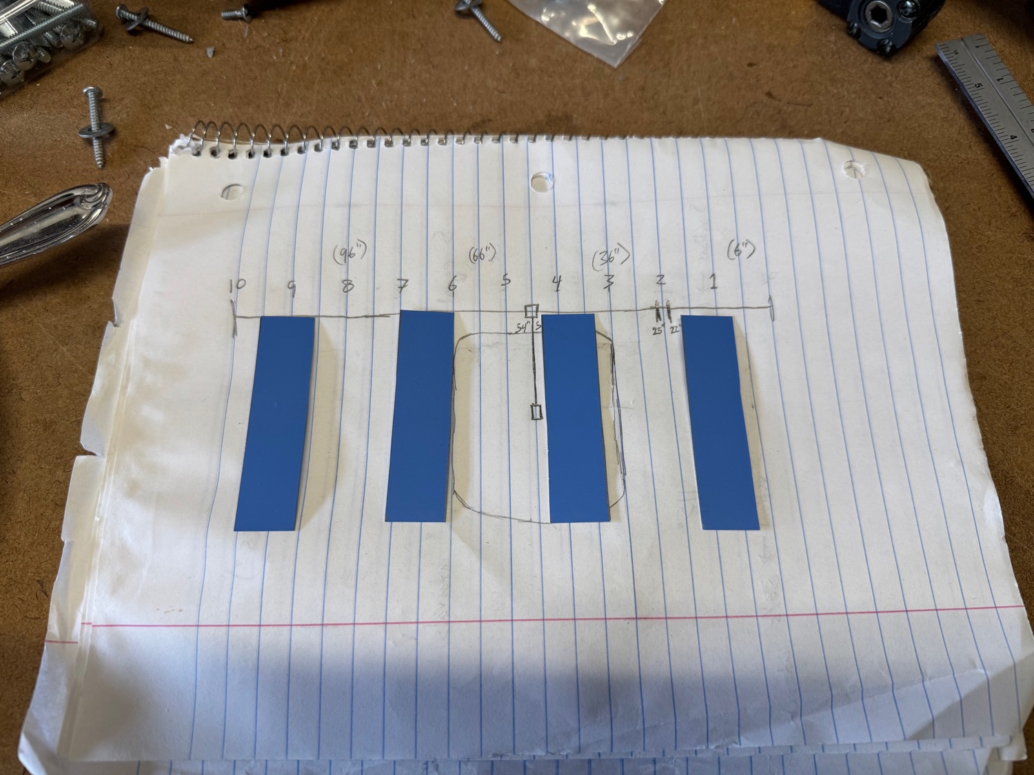 A built-in layout sketched on lined paper with movable blue paper cut-outs and spacing marked in inches — the design externalized and rearranged before any wood is cut