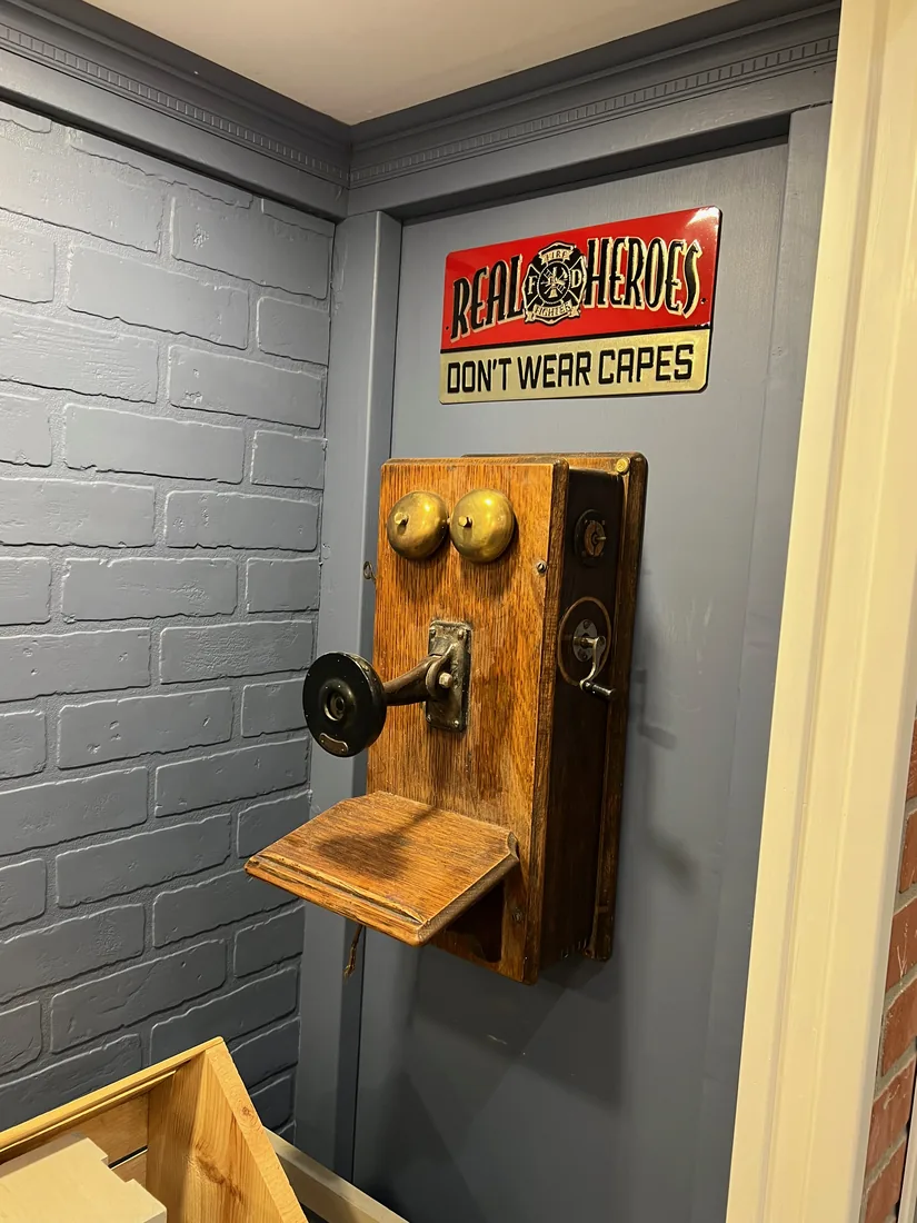 A vintage wooden wall telephone and a 'Real Heroes' tin sign decorating the Fire Station's interior brick