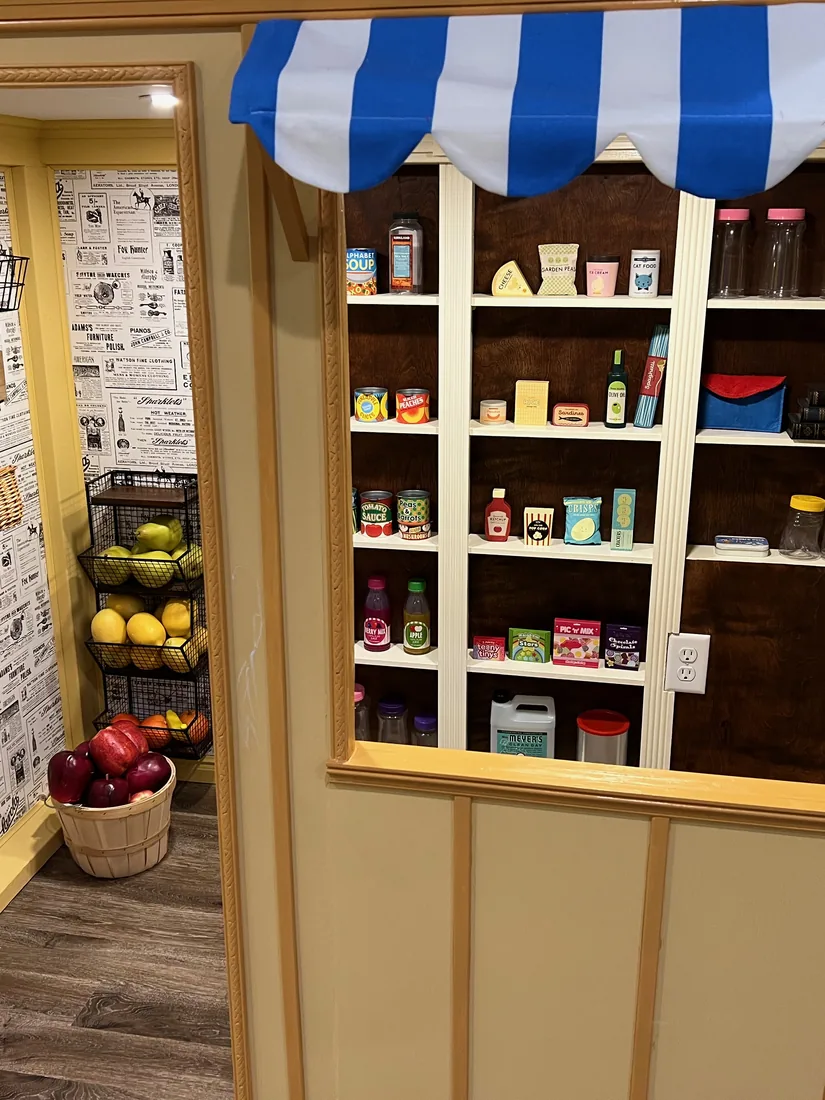 Inside the Grocer — a register window under a blue-striped awning, flanked by built-in shelves