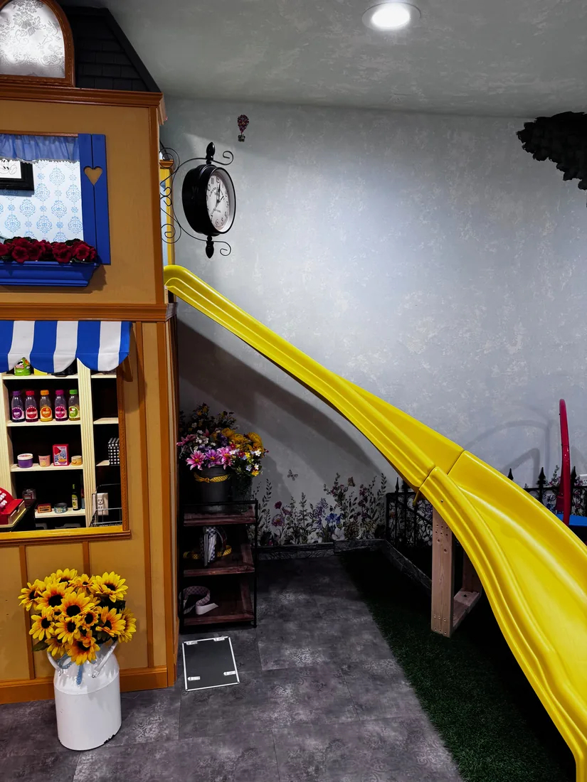 A slide running down the side of the Peterson Grocer beside the storefront and a station clock