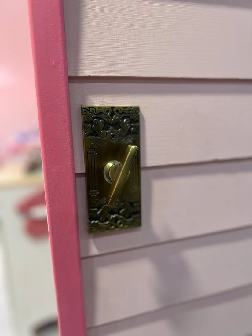 A brass antique doorbell mounted beside Rose Cottage's pink lap siding