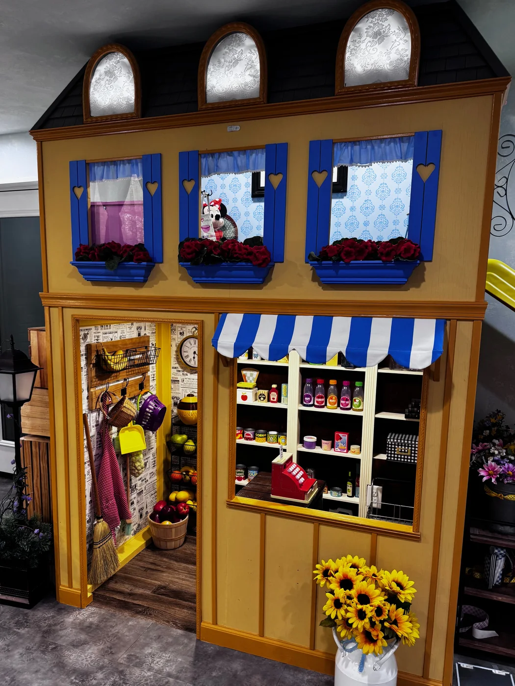 The Peterson Grocer playhouse — a yellow two-story storefront with arched windows, a striped awning, and a register counter