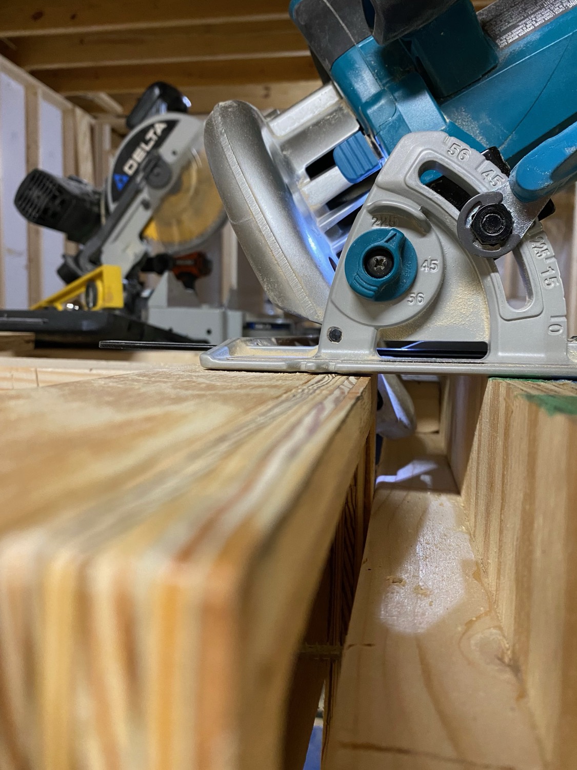 A circular saw resting on a stack of laminated beams with a miter saw in the background — the two saws this guide is built around