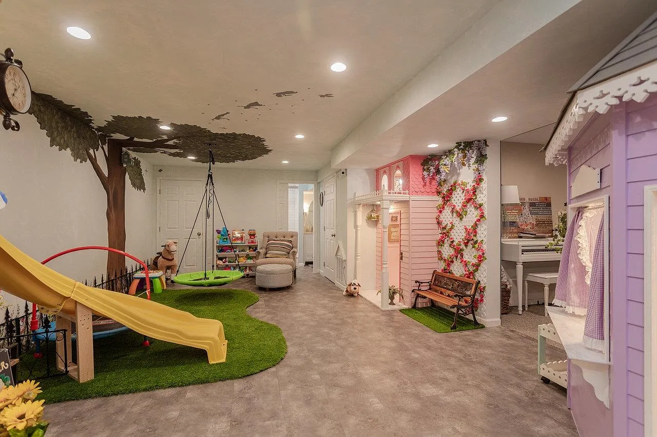 Victorian village from across the room — slide, painted tree, swing, and four playhouses